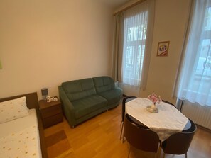 Ein Zimmer mit einem grünen Sofa, einem kleinen Tisch mit weißer Tischdecke und einem Bett mit weißer Daunendecke.