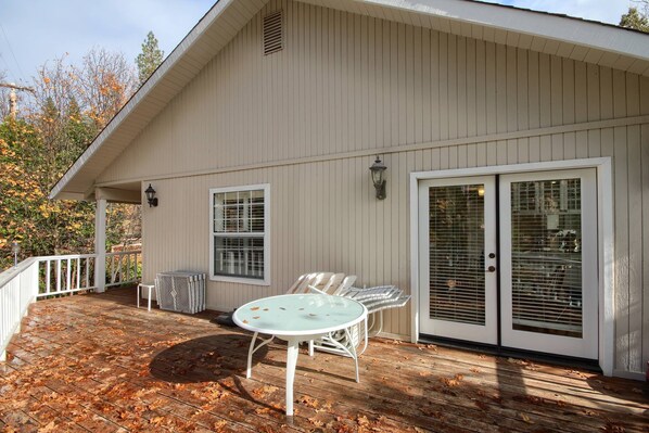 A covered deck with a table and chairs, a sliding glass door, and a white exterior wall.