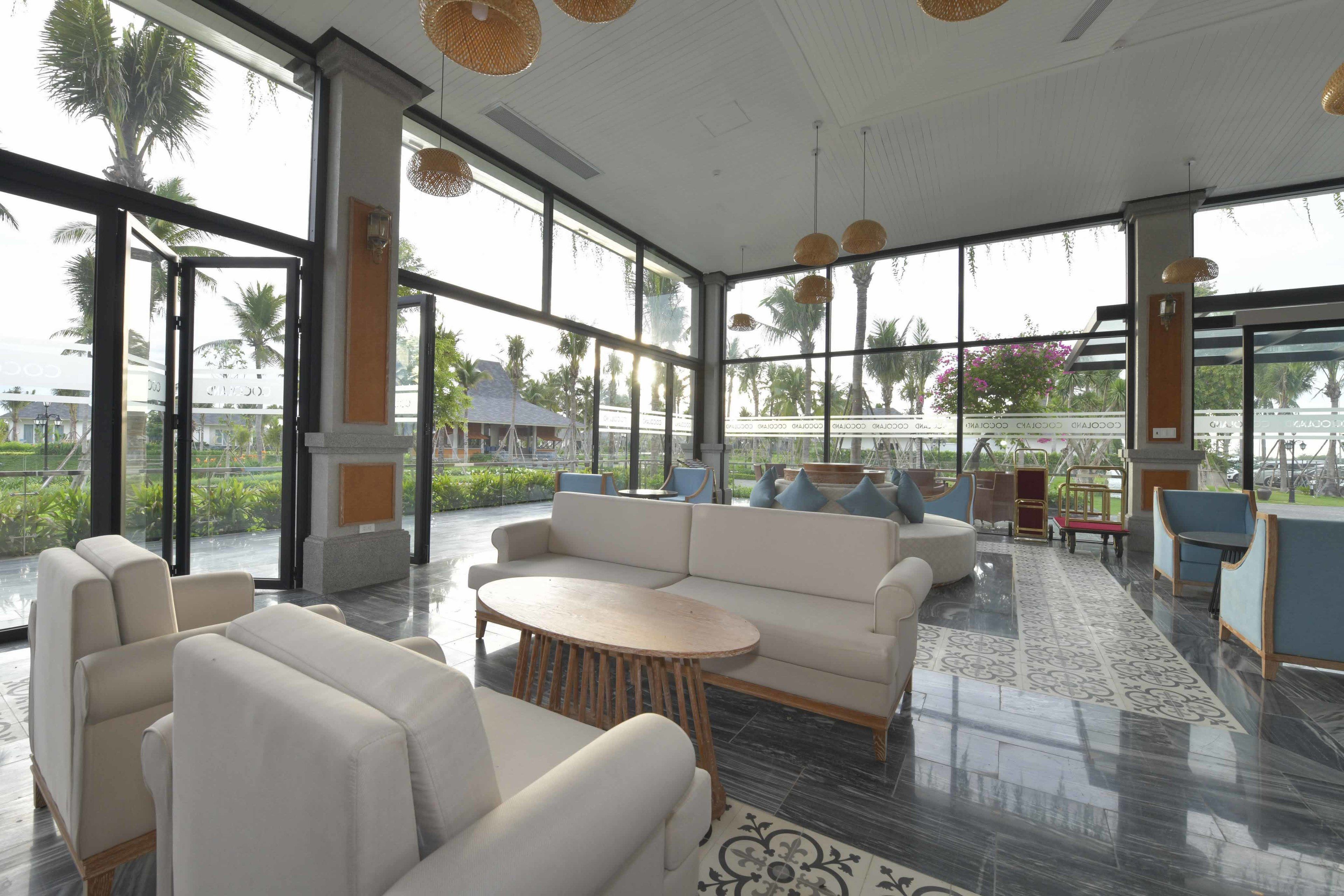 A spacious indoor area with a large window, a sofa, a round table, and a patterned rug.