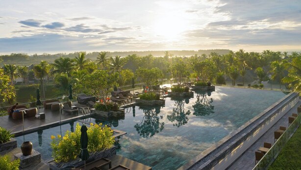 A infinity pool with lounge chairs and planters, surrounded by palm trees and a view of the horizon. - Cocoland River & Beach Resort (Tu Nghia)