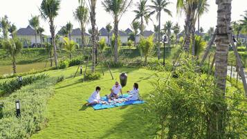 A group of people having a picnic on a grassy area surrounded by palm trees and a body of water.