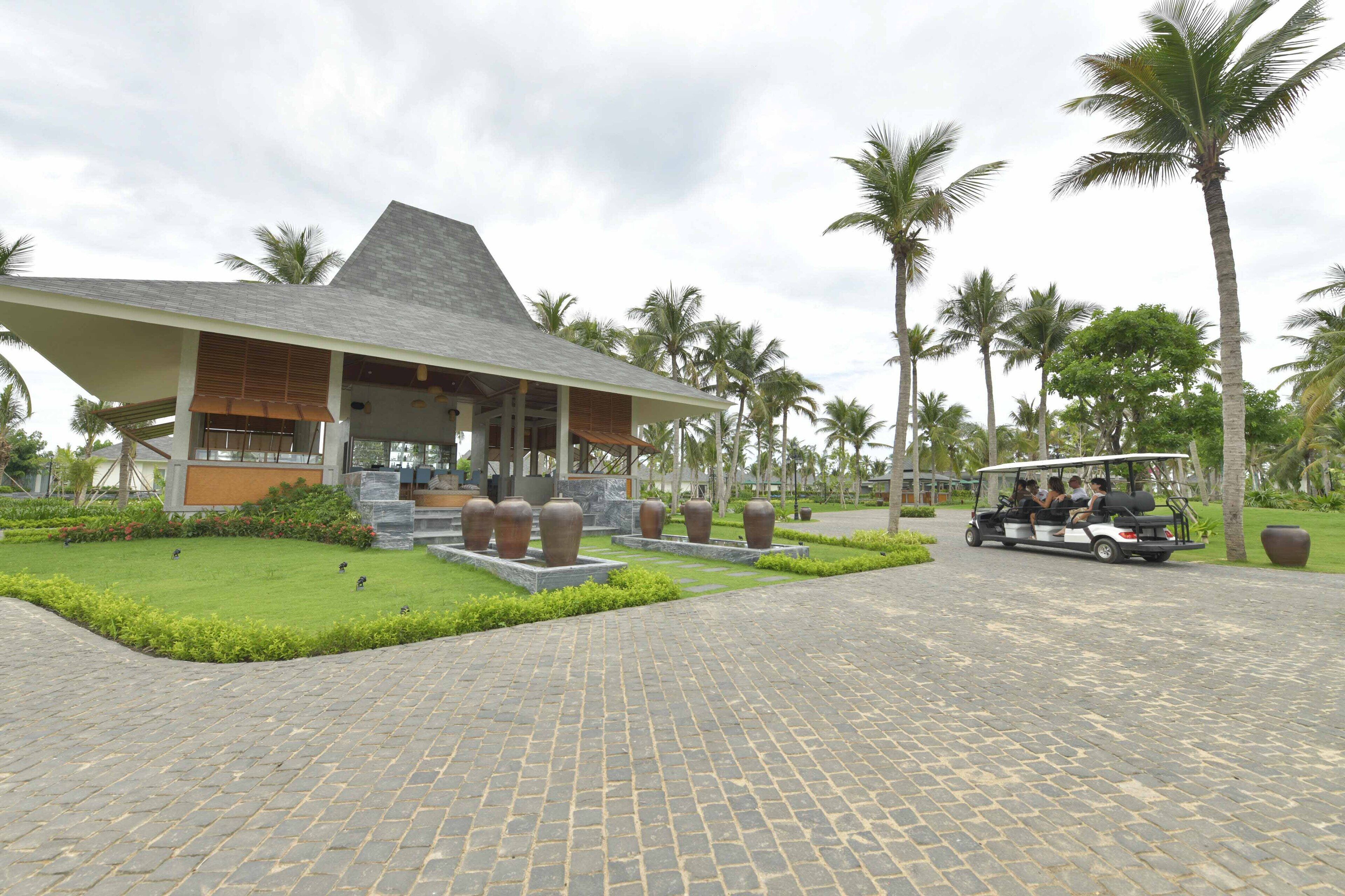 A modern building with a sloped roof, surrounded by palm trees and a paved walkway.