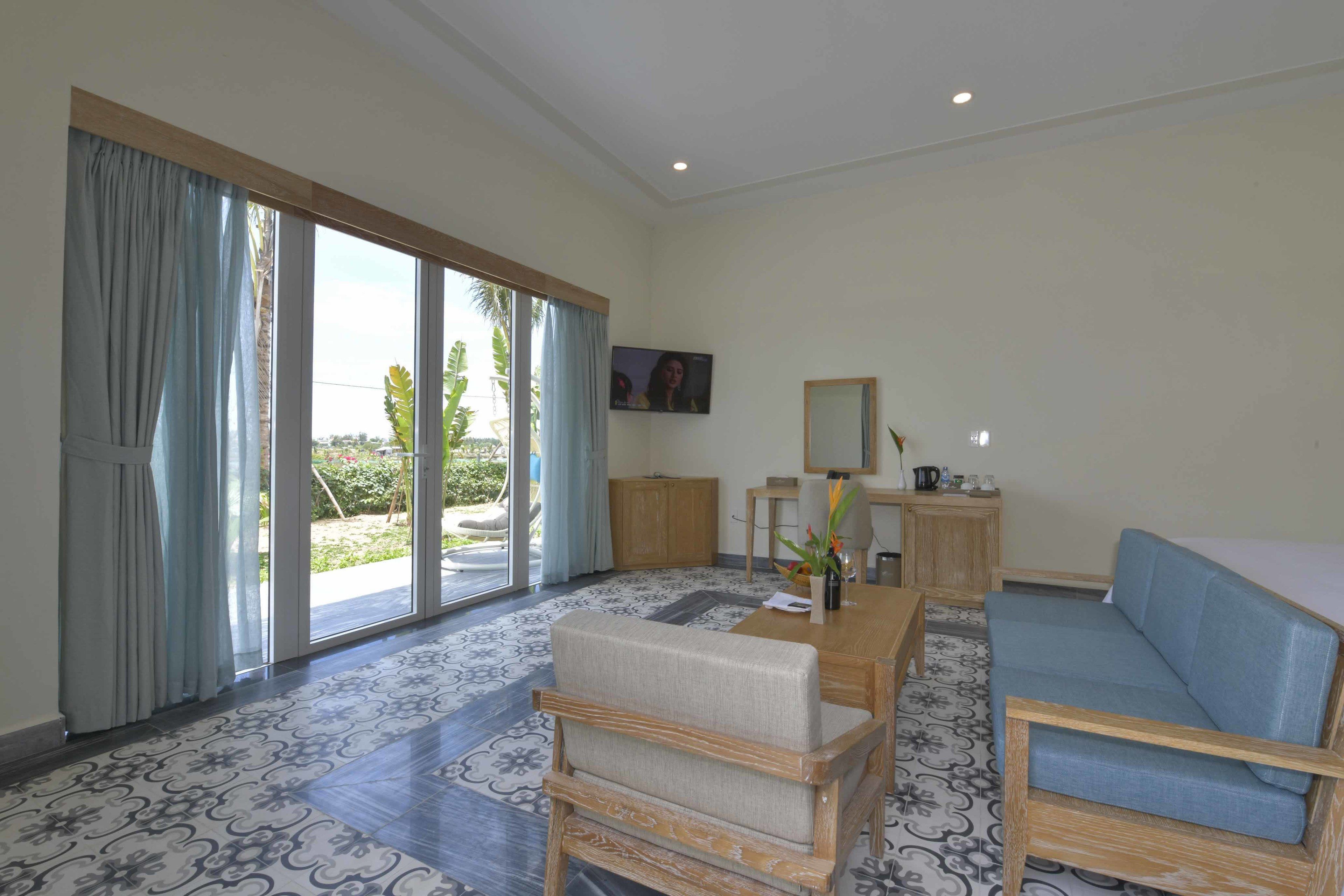 A spacious room with a large sliding glass door leading to a garden, a sofa, a wooden coffee table, and a television mounted on the wall.