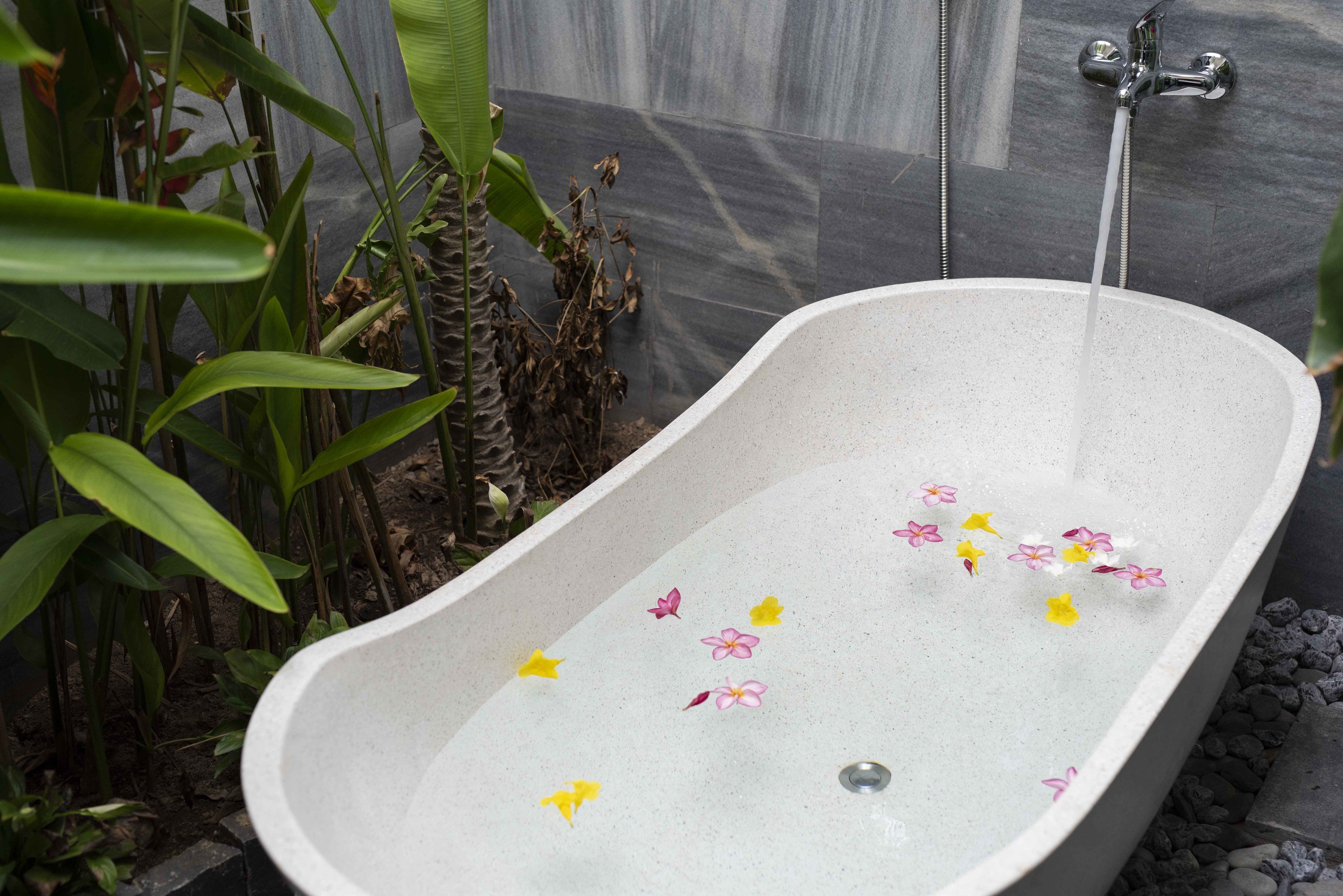 Una bañera independiente con agua corriendo, rodeada de plantas y un muro de azulejos.