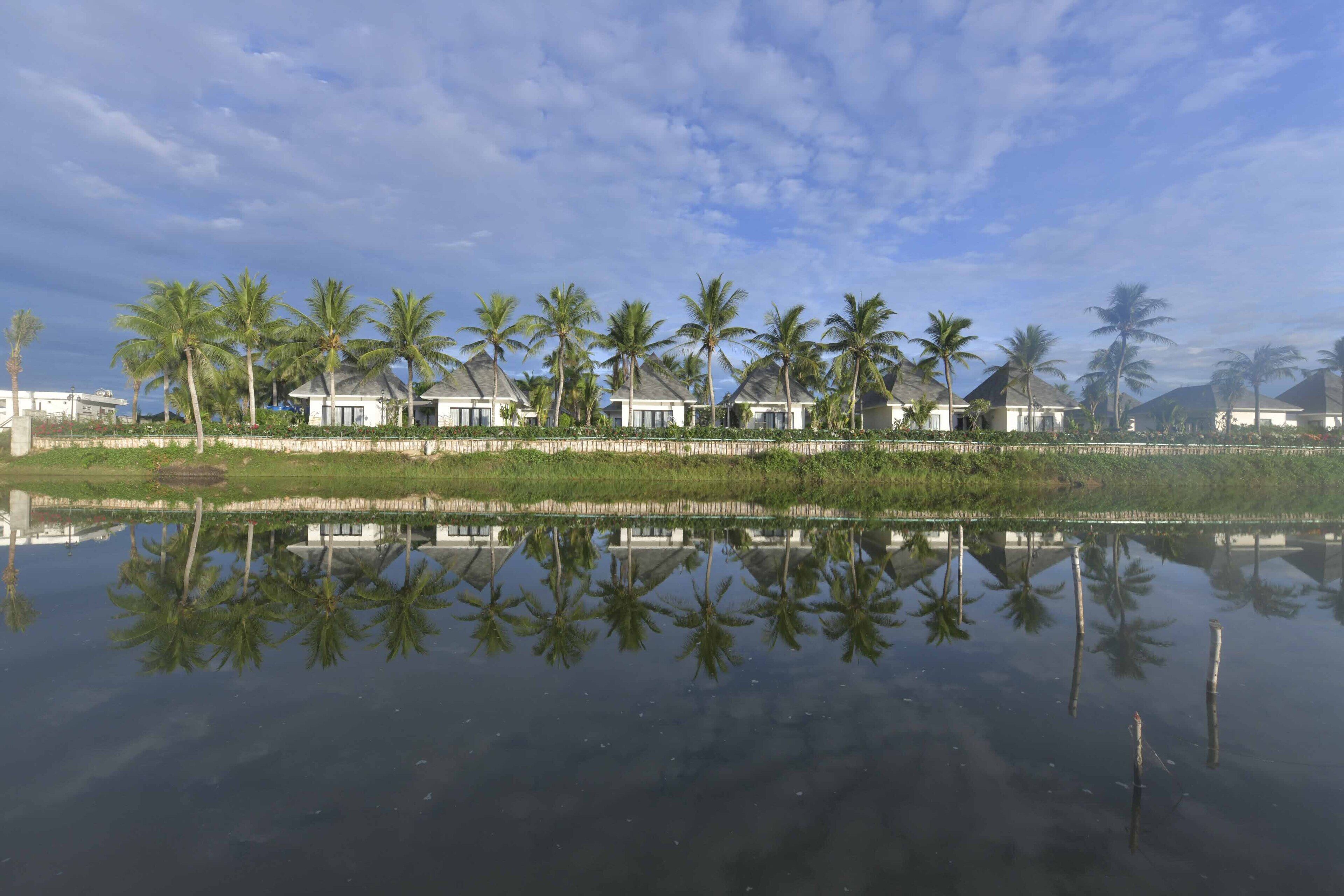 A waterfront property with multiple houses, palm trees, and a calm reflective water surface.