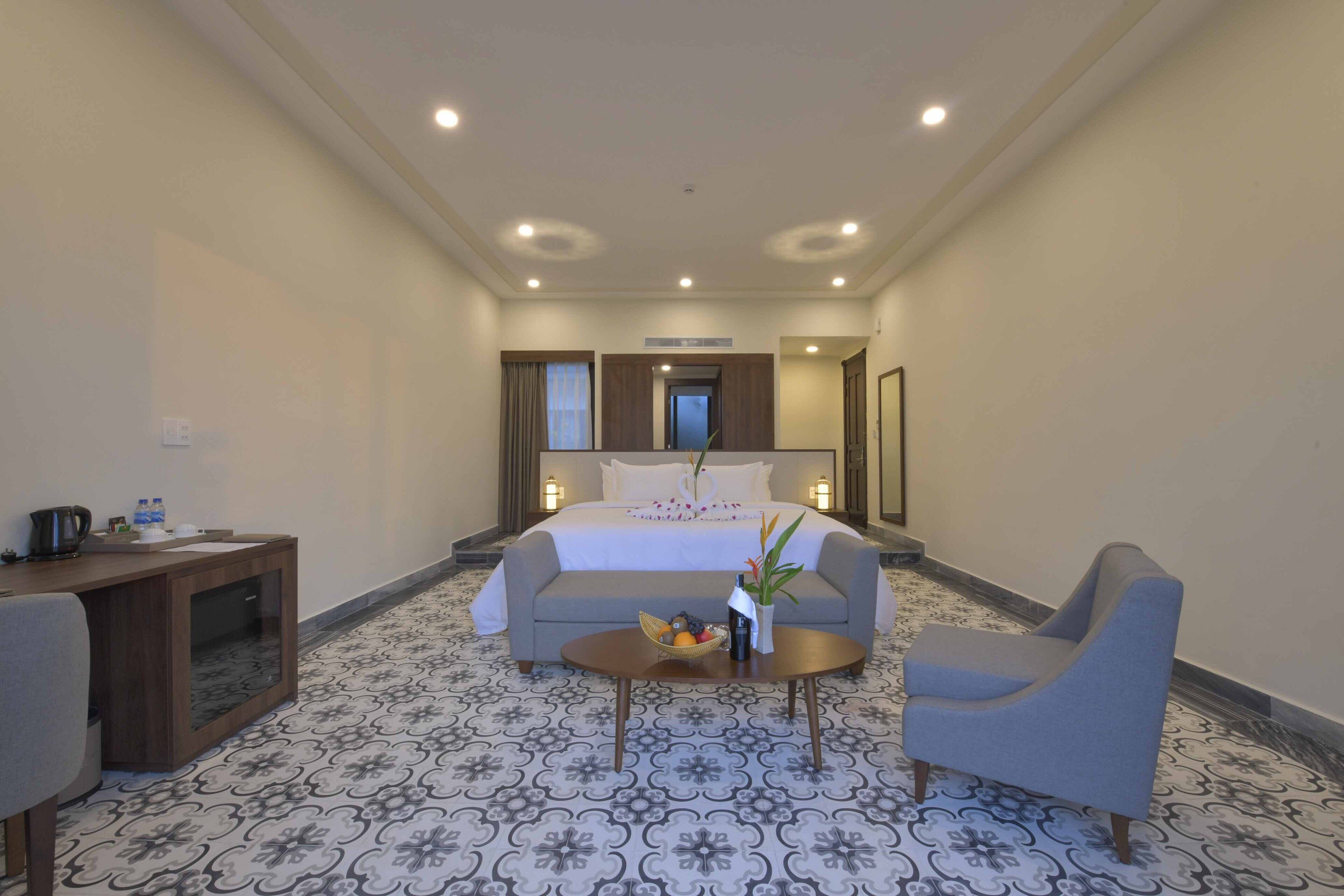 A hotel room with a bed, a desk, a coffee table with fruit, and two armchairs.