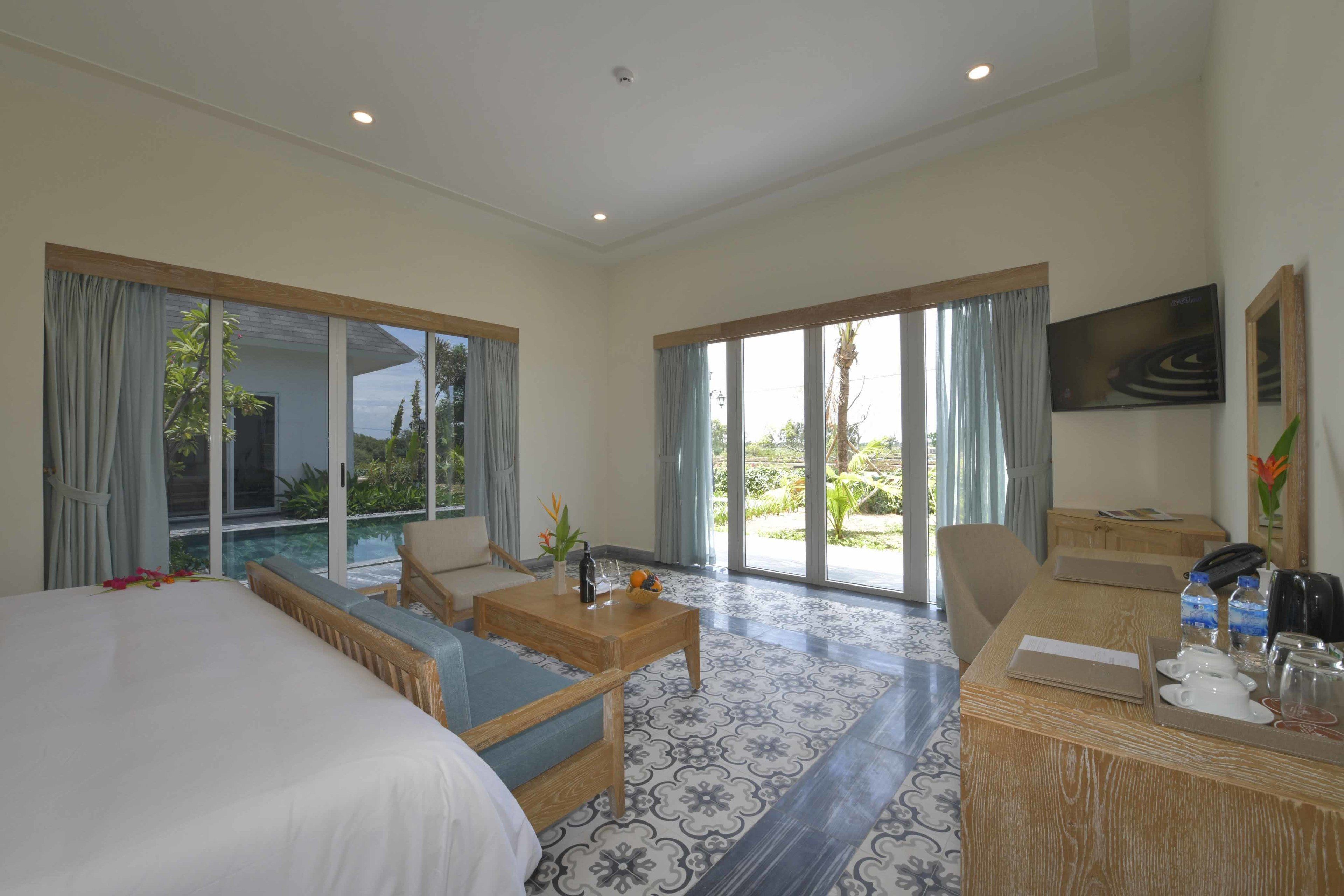A hotel room with a bed, a sofa, a desk with amenities, and large sliding glass doors to an outdoor area.