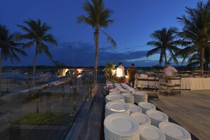 Un restaurante frente al mar con terraza, palmeras y vistas al océano.