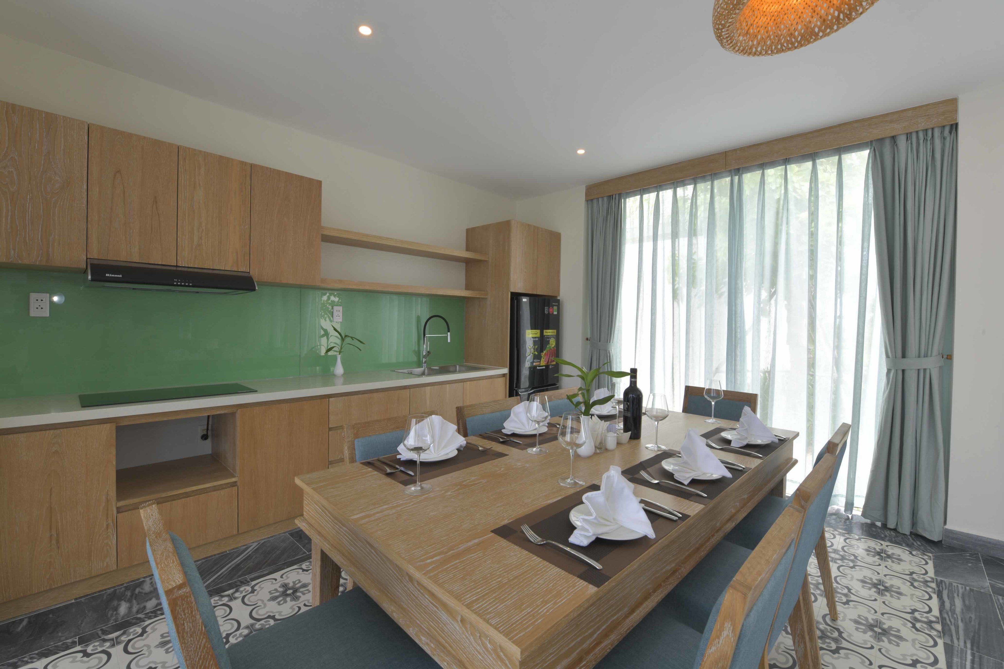 Een moderne eetruimte met een houten tafel voor zes personen, een keuken met houten kastjes, en een groot raam met gordijnen.
