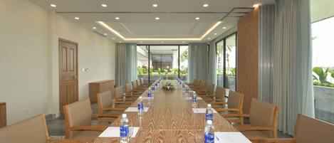 Un salón de conferencias con una larga mesa de madera, varias sillas y botellas de agua.