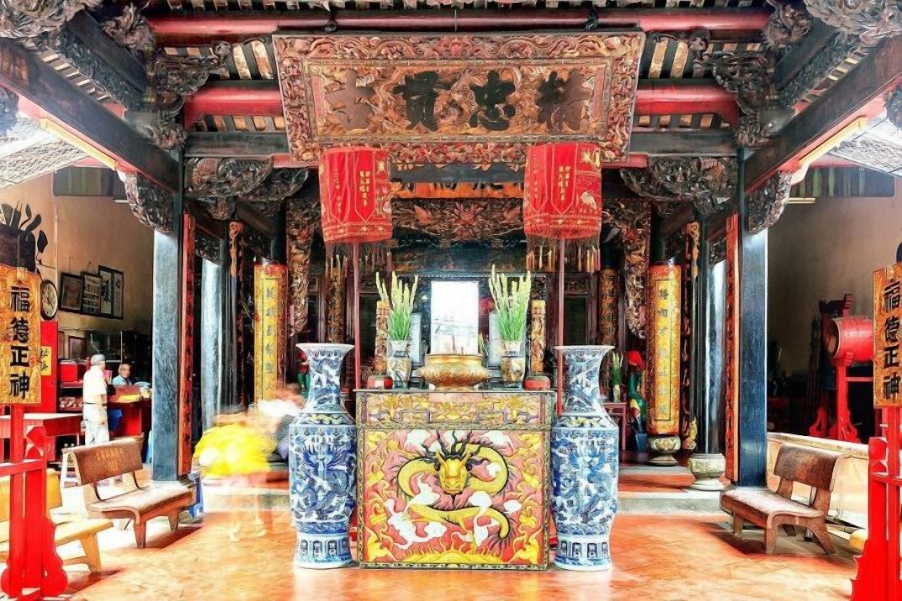 L’intérieur d’un temple richement décoré, présentant une architecture chinoise traditionnelle, avec des sculptures complexes et des lanternes rouges.