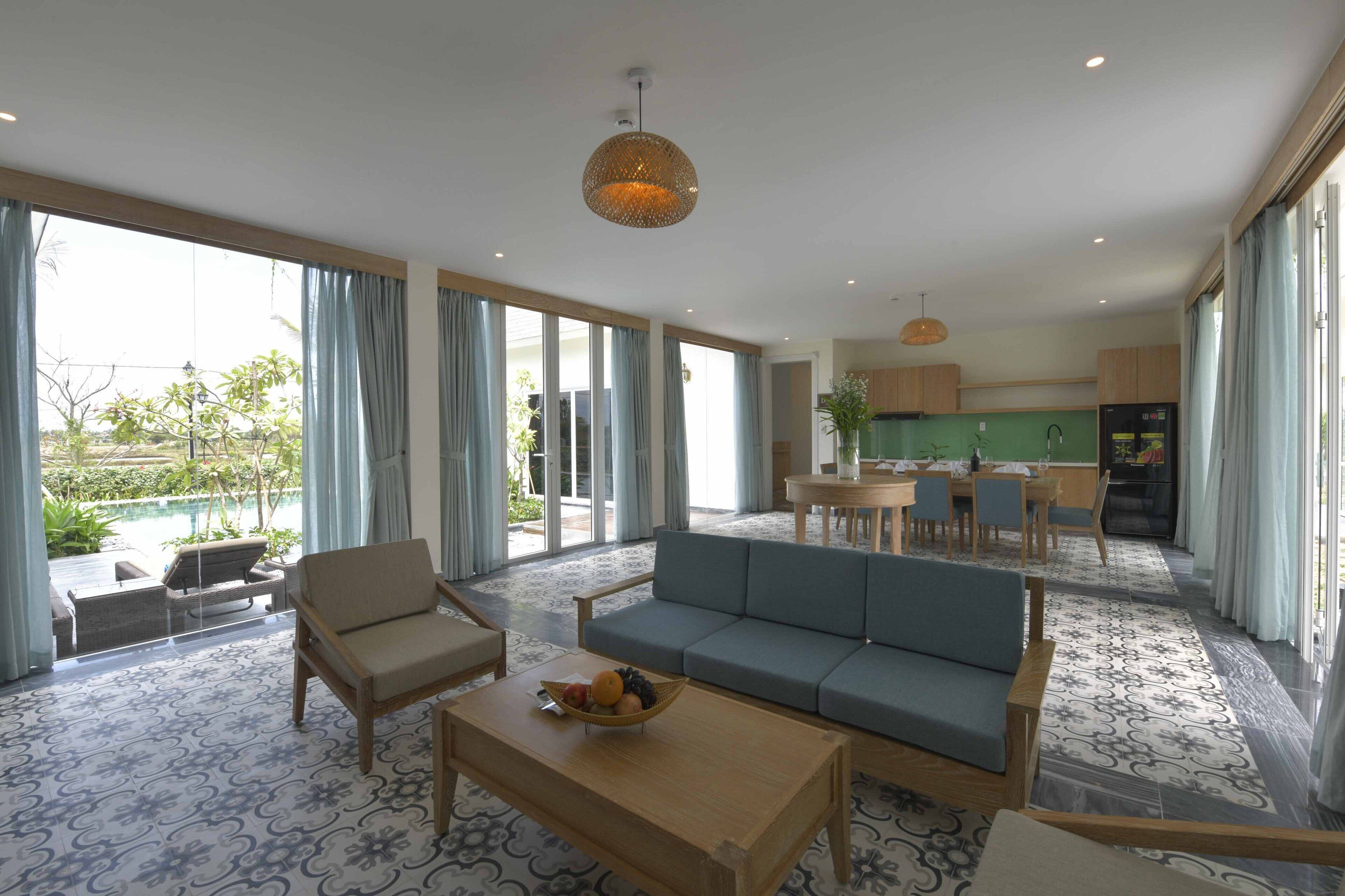 Ein großzügiger Wohnbereich mit Sofa, Sesseln und Couchtisch. Es gibt einen Essbereich mit Tisch und Stühlen, und im Hintergrund eine Küche.