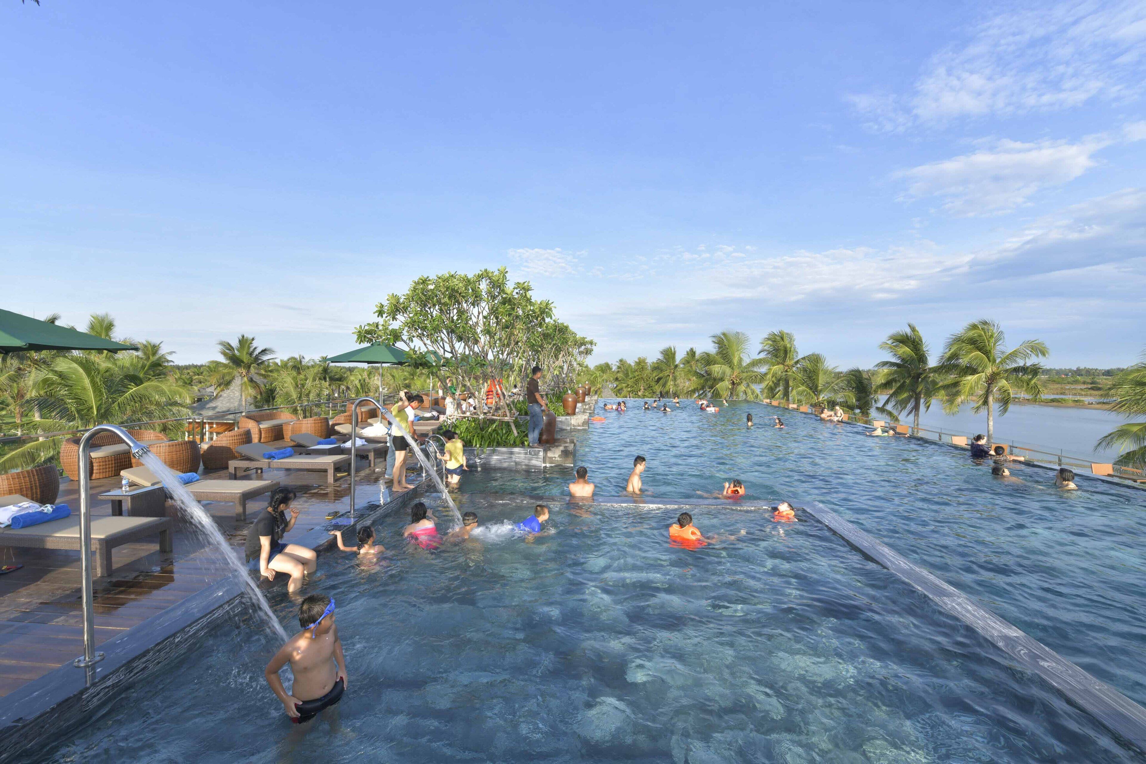 Ein Poolbereich mit Liegestühlen und Sonnenschirmen, umgeben von Palmen und blauem Himmel.