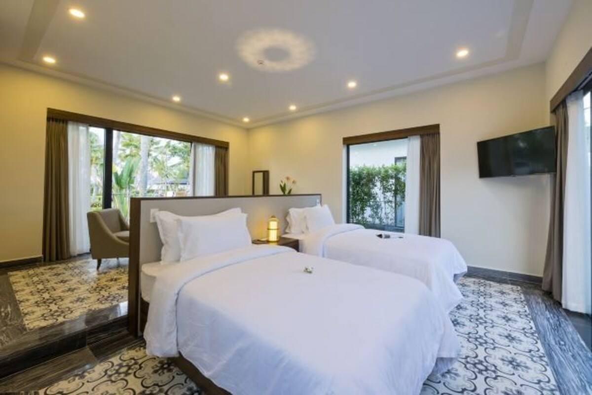Habitación de hotel con dos camas, televisión, una silla y vista a zonas verdes.