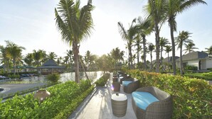 A pathway lined with wicker furniture and palm trees, leading to a body of water. - Cocoland River & Beach Resort (Tu Nghia)