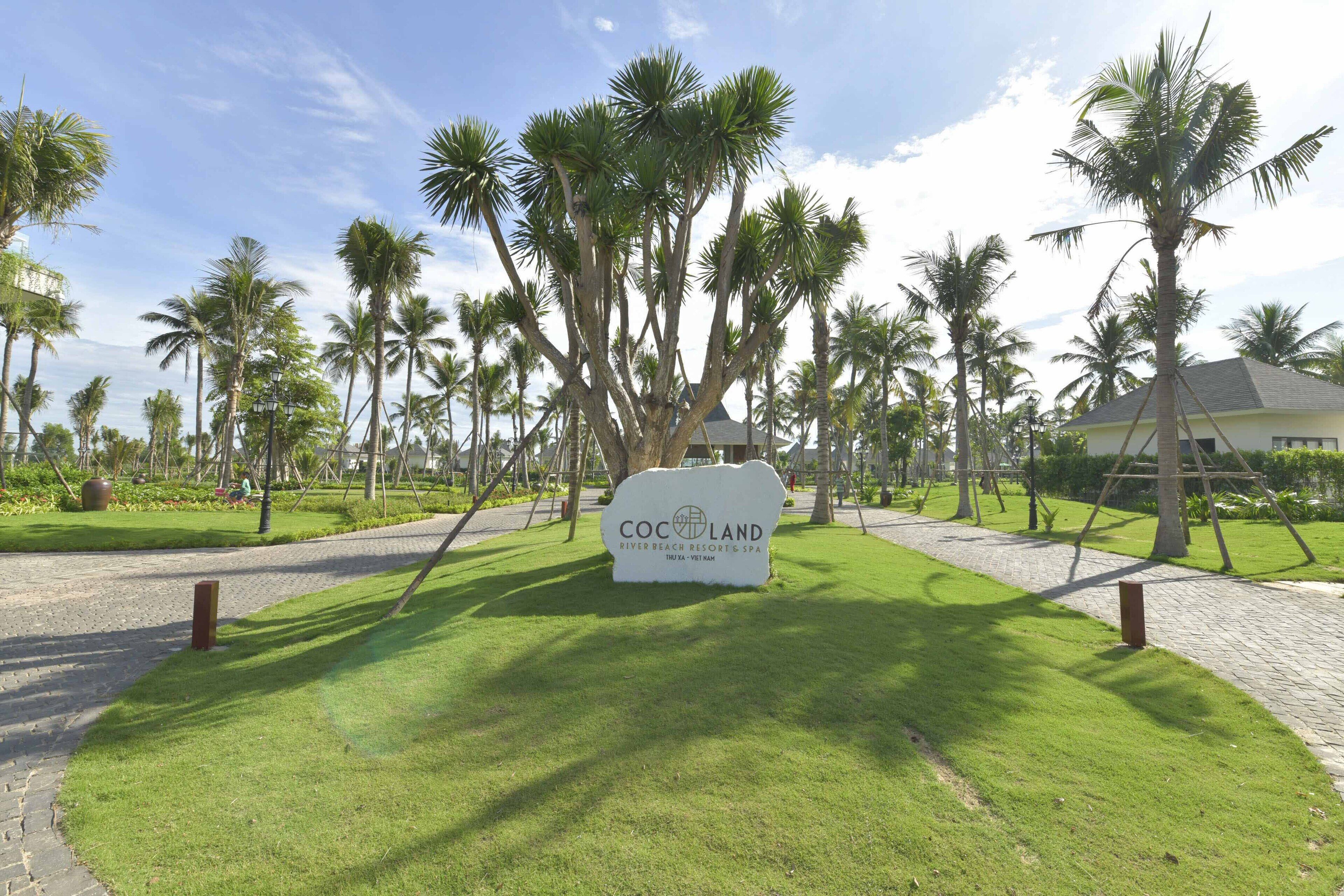 Señal de Cocoland River Beach Resort & Spa con un camino pavimentado y palmeras.