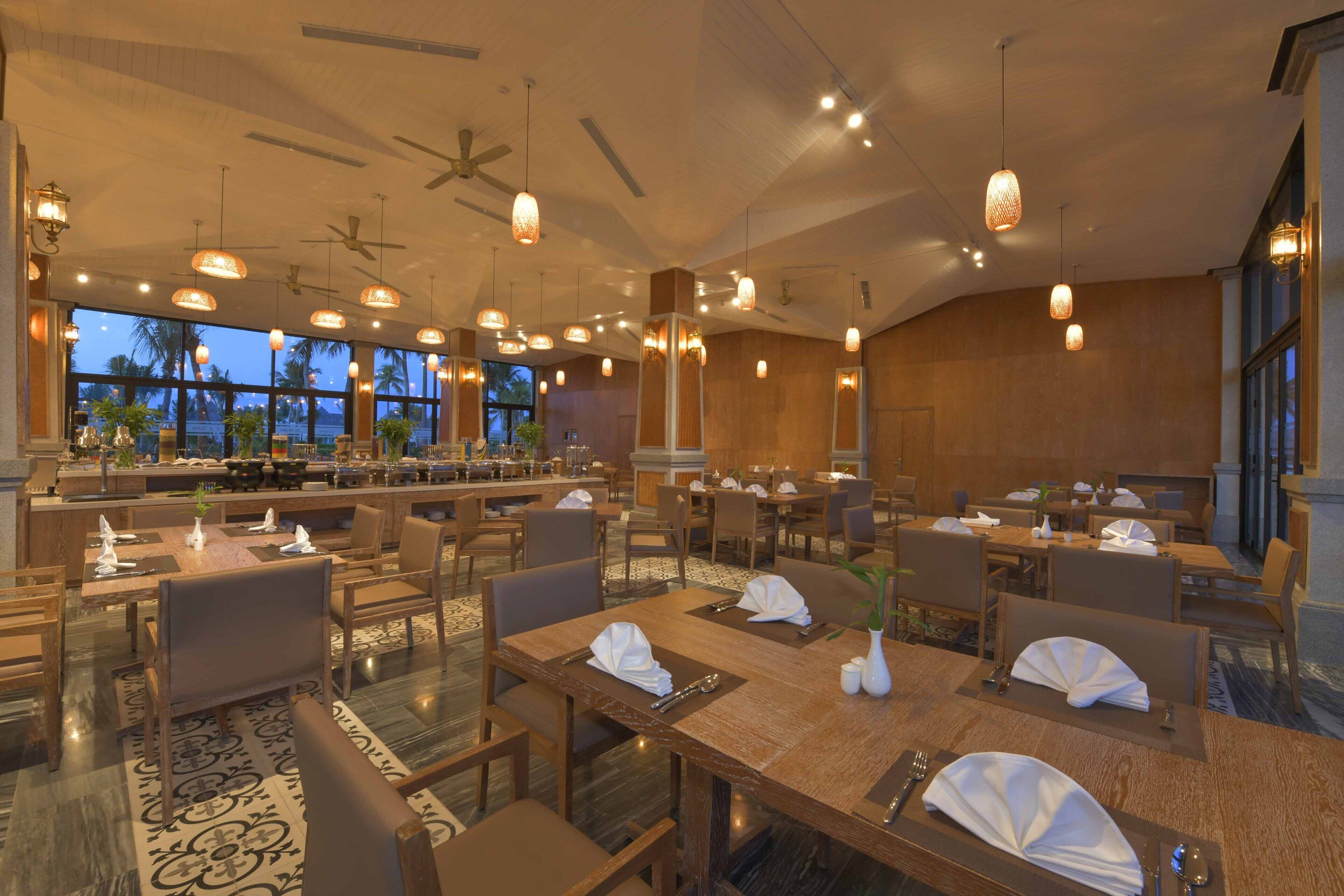 A spacious restaurant with multiple dining tables, chairs, and hanging pendant lights.