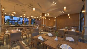 A spacious restaurant with multiple dining tables, chairs, and hanging pendant lights.