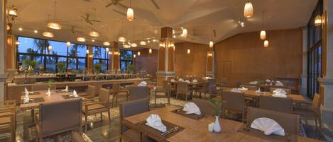 A spacious restaurant with multiple dining tables, chairs, and hanging pendant lights.