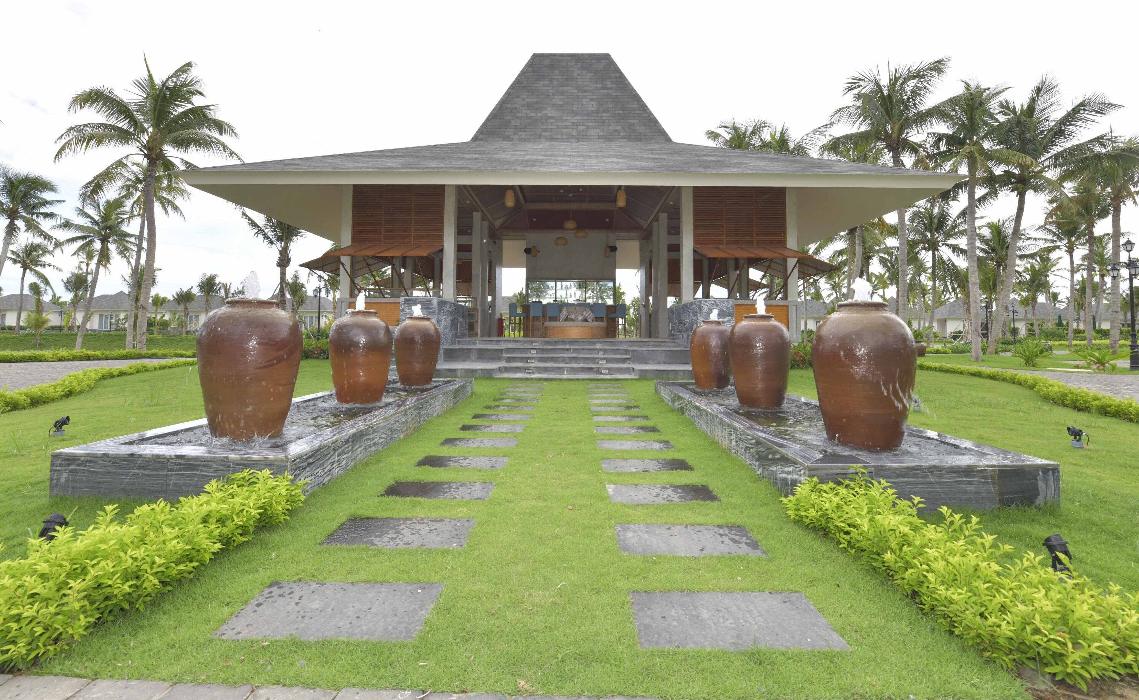 A hotel entrance with a covered walkway, large vases, and a well-maintained lawn.