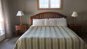 Un dormitorio con cama, dos mesitas de noche, una ventana con persianas y una silla.