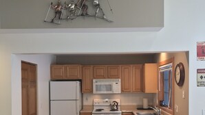 Cocina compacta con armarios de madera, un refrigerador, un microondas, una tetera y dos taburetes de bar.