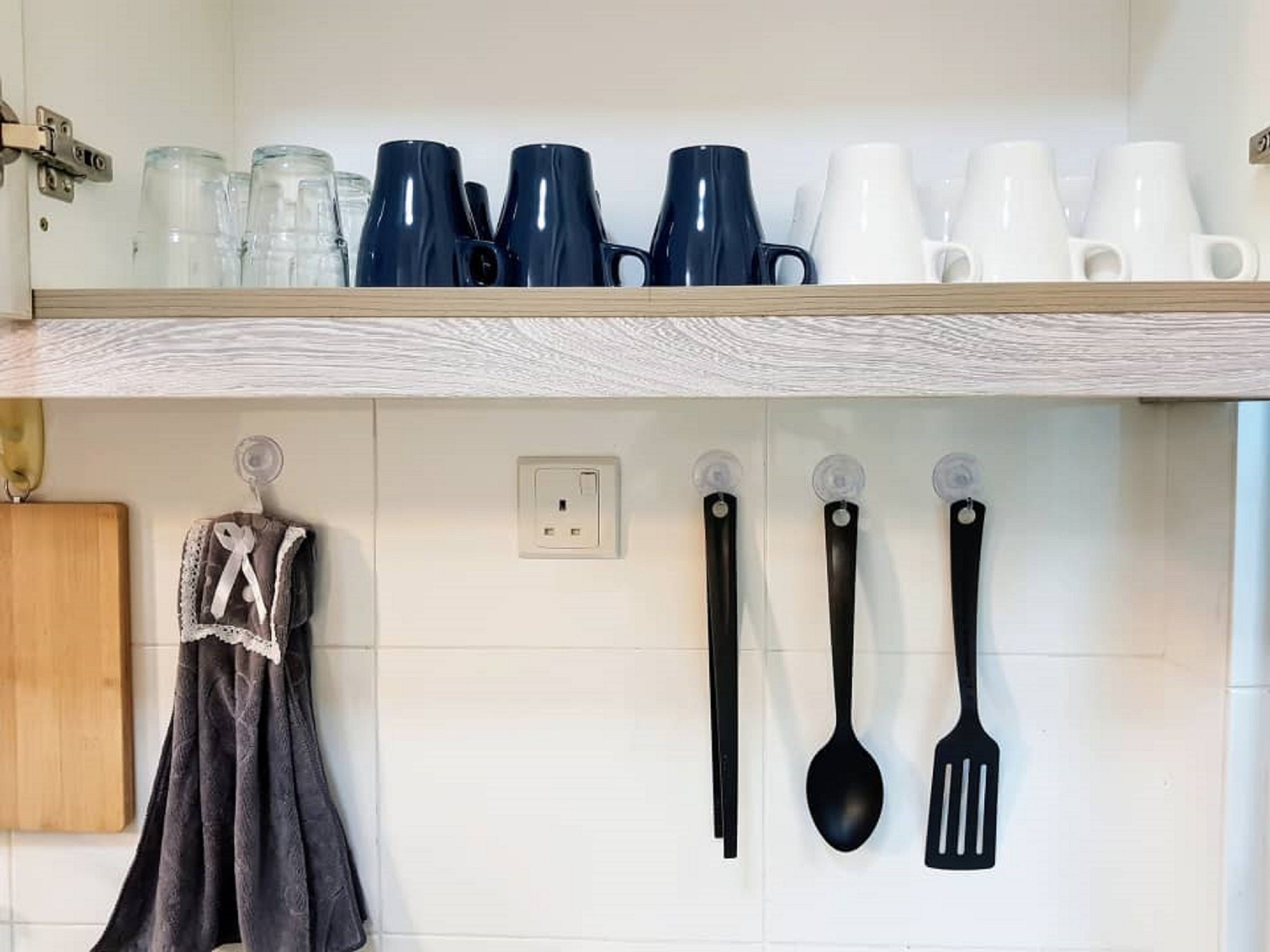 Ett kök med en hylla i trä där olika typer av muggar och glas står, och ett knivblock som är fäst på väggen med köksredskap i.