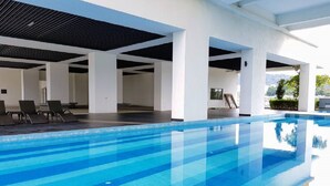 Une piscine à l’eau d’un bleu cristallin, entourée de piliers blancs et dotée d’un espace abrité avec des chaises longues.