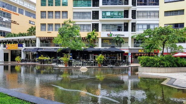 Une cour intérieure agrémentée d’une fontaine centrale, entourée de bâtiments abritant différents commerces, notamment un café et des restaurants.