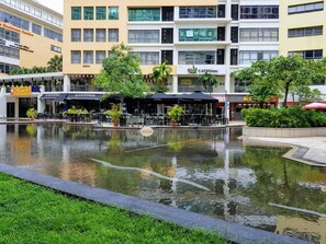 A courtyard with a central water feature, surrounded by buildings with various storefronts, including a coffee shop and restaurants. - Setiawalk by TL (Puchong)