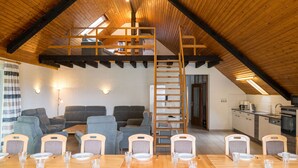 A spacious loft with a high ceiling, wooden beams, a dining area with a long table and chairs, a kitchen, and a loft bedroom with a wooden ladder. - Eifelnatur (Haus 2) by Interhome (Immerath)