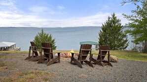 Uma área de estar à beira do lago, com cadeiras Adirondack e uma lareira, com vista para um lago calmo.