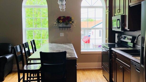 A modern kitchen with a central island, stainless steel appliances, and large windows. - Mona K's-Little Green Rental (Green Lake)