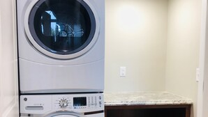 A laundry room with two stacked front-loading washing machines and a shelf below containing a red toy and a white laundry basket. - Mona K's-Little Green Rental (Green Lake)