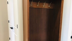 A wooden wardrobe with a bench and hooks, a white door with a black handle, and a wooden floor. - Mona K's-Little Green Rental (Green Lake)