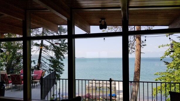 Een kamer met grote ramen en uitzicht op een wateroppervlak, een balkon met stoelen en een zeezicht.