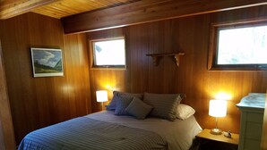 Een slaapkamer met houten lambrisering, een bed, twee bedlampen en een nachtkastje.