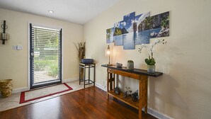 A hallway with a wooden floor, a door with blinds, a small table with a bowl and plants, and a wall with framed pictures. -  Family & Pet Friendly (*additional pet fee will apply), Charming Orlando Home! (Orlando)