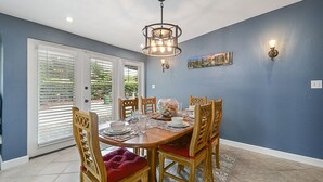A dining area with a round table, six wooden chairs with red cushions, a chandelier, and a cityscape painting on the wall. -  Family & Pet Friendly (*additional pet fee will apply), Charming Orlando Home! (Orlando)