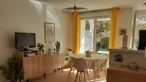 Eine moderne Küche mit Essbereich, einem Fernseher auf einem Holzschrank und einem Fenster mit gelben Vorhängen.
