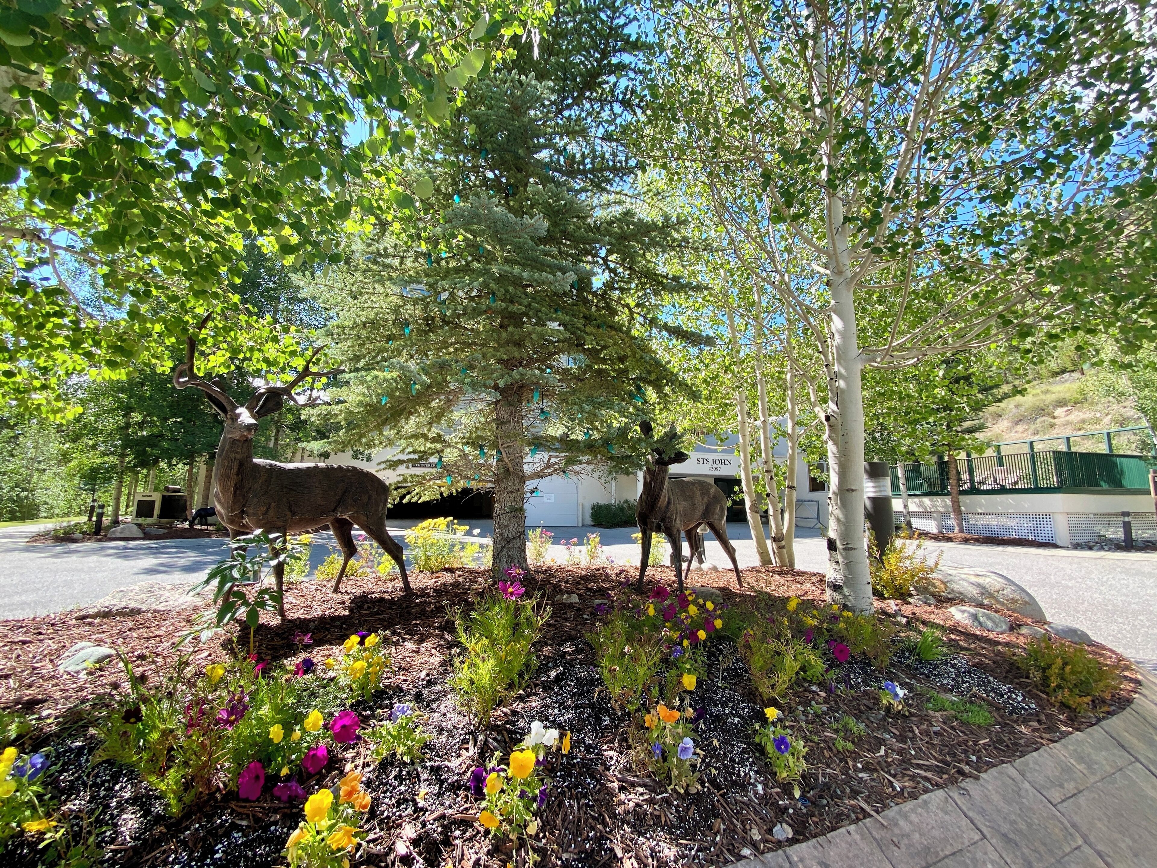 A landscaped area with deer statues, trees, and colorful flowers.