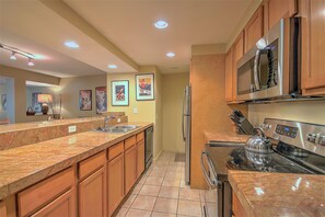 A modern kitchen with granite countertops, stainless steel appliances, wooden cabinets, and recessed ceiling lighting.