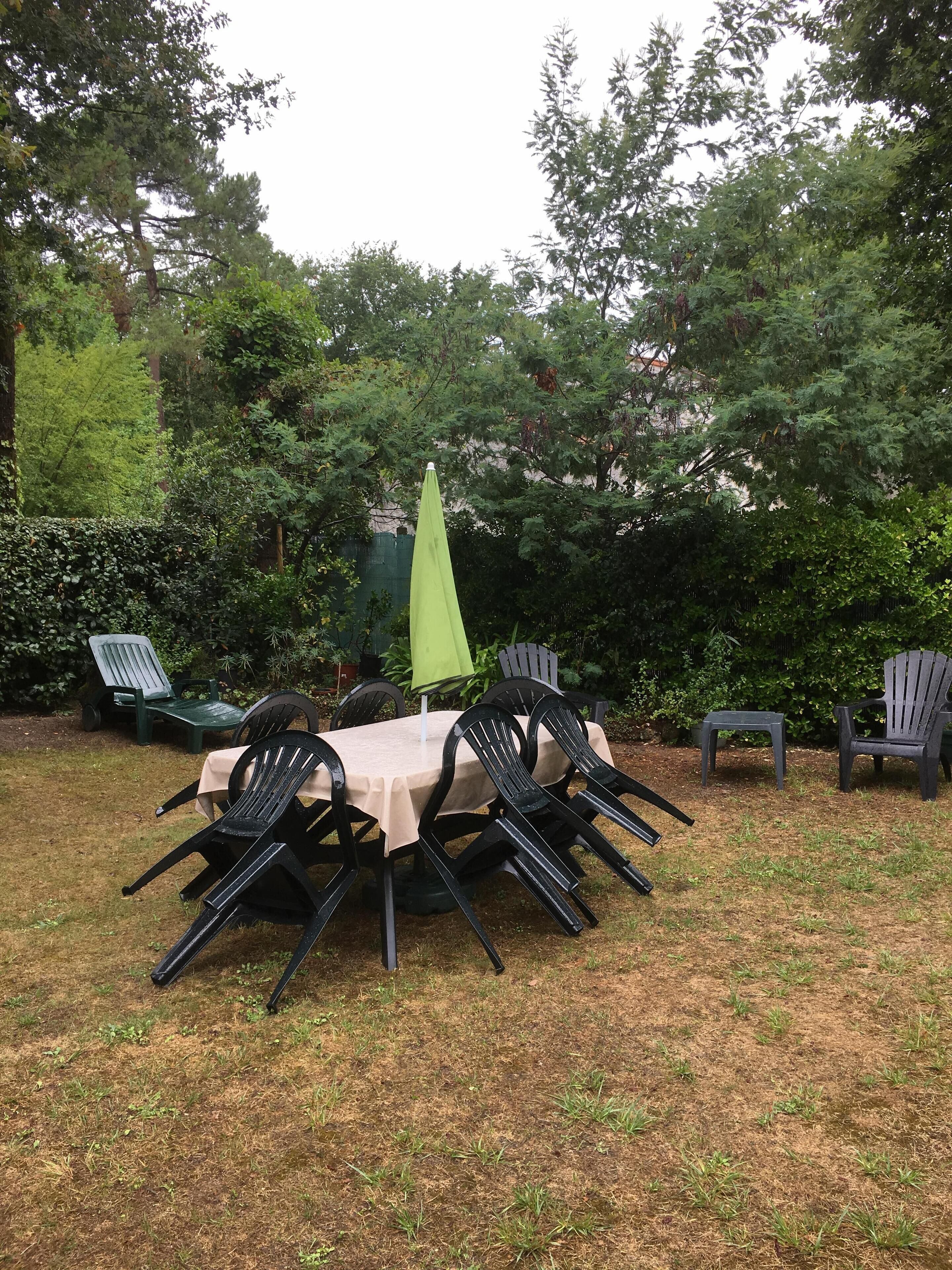 Une terrasse extérieure avec une table ronde et des chaises, entourée de verdure et d’arbres.