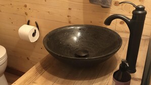 A wooden sink with a black faucet, a toilet paper holder, and a bottle on the counter.