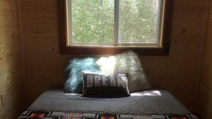 A room with a bed, a window, and a view of trees outside.