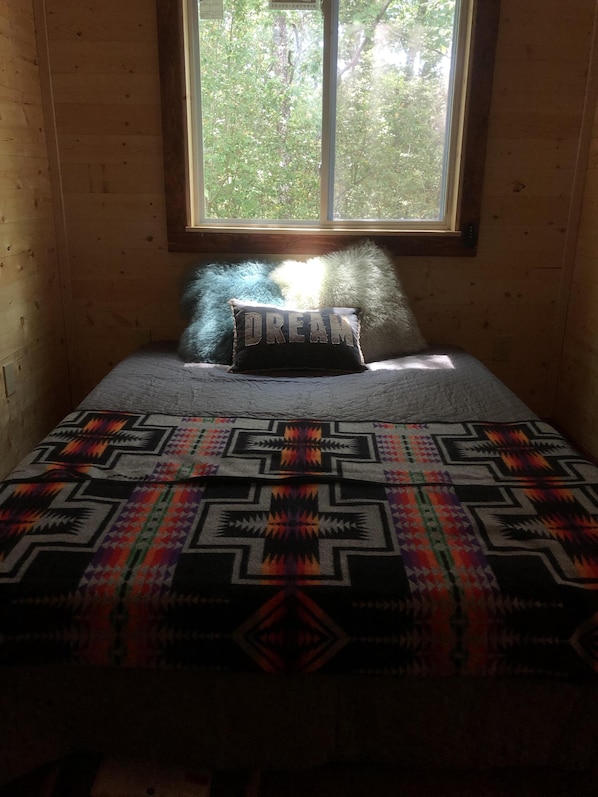 A room with a bed, a window, and a view of trees outside.