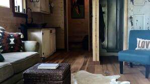 A cozy cabin interior with a wooden ceiling, a sofa, a wicker ottoman, a fur rug, and a blue chair with a 'LOVE' cushion.