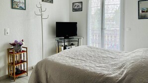 A bedroom with a bed, a television on a stand, a window with a view, and a wall-mounted coat rack. - Central T2 Apartment with Terrace, Cambo-les-Bains (Cambo-les-Bains)
