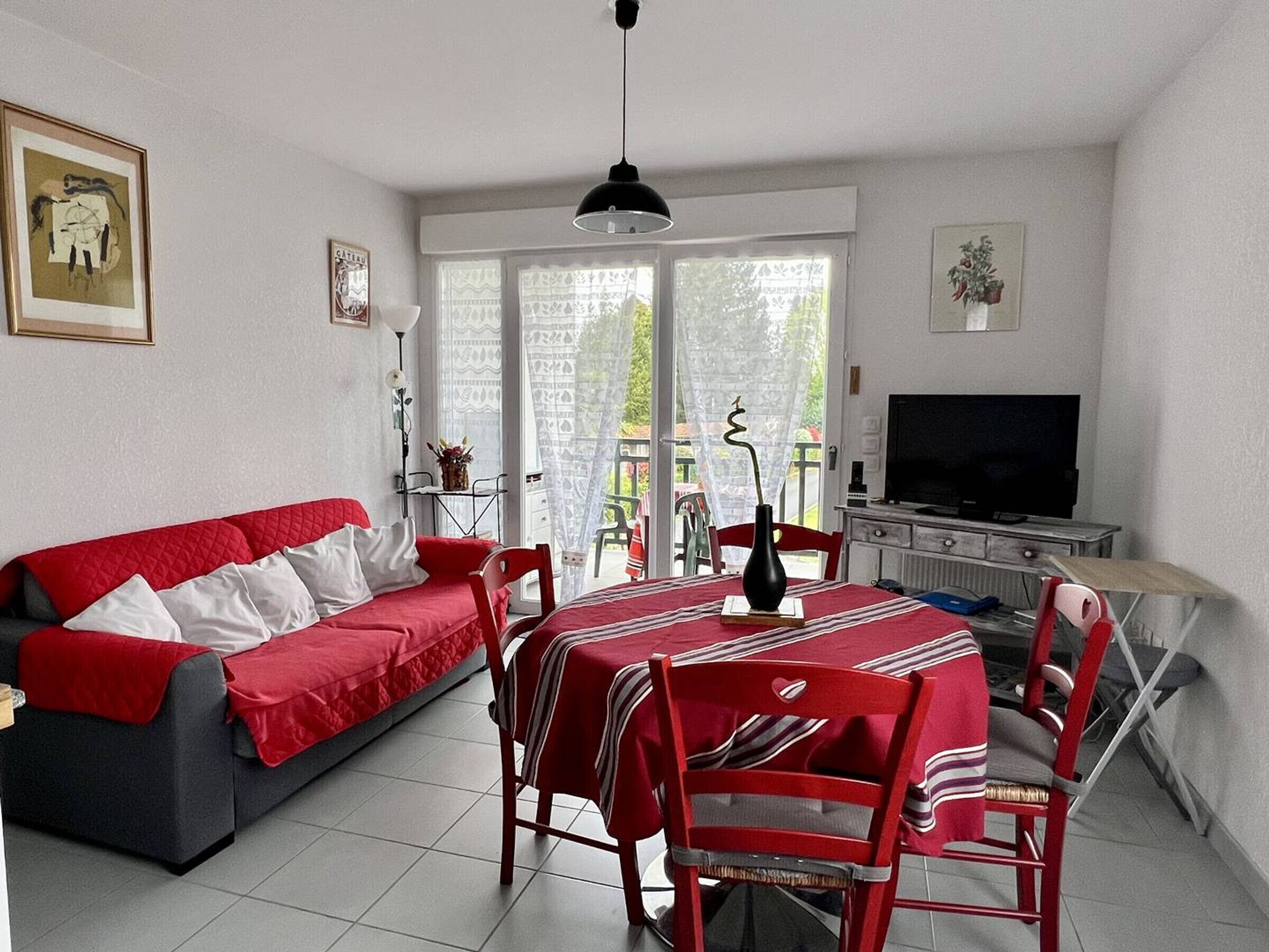 En stue med en rød sofa, et spisebord med stole, et fjernsyn og en balkon med udsigt.