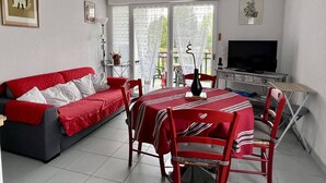 A living room with a red sofa, a dining table with chairs, a TV, and a balcony with a view. - Central T2 Apartment with Terrace, Cambo-les-Bains (Cambo-les-Bains)